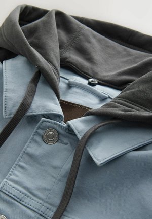 Blauwe en grijze ritsvest met capuchon, voorzien van een knoopsluiting, trekkoorden en contrasterende stoffen texturen bij de kraag en capuchon.