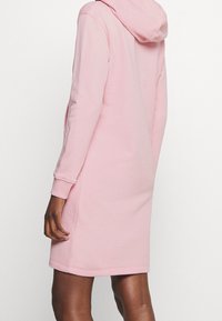 Vestido sudadera de algodón rosa con mangas largas, bolsillos laterales y un ajuste relajado. Cuenta con capucha con cordón y puños acanalados en las muñecas.