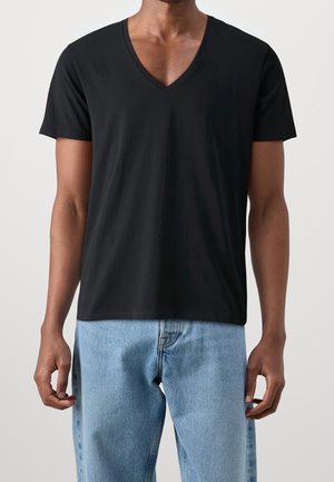 Man wearing a plain black short-sleeve V-neck T-shirt paired with light blue denim jeans, standing against a plain background.