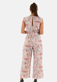 Un mono floral en rosa con lunares, que cuenta con mangas cortas, un escote en la espalda y una cintura ceñida con cinturón. La tela tiene una textura ligera.