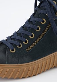 Baskets montantes en cuir vert foncé avec des lacets marine, des œillets dorés et une fermeture éclair sur le côté. Présente une semelle en caoutchouc texturé.