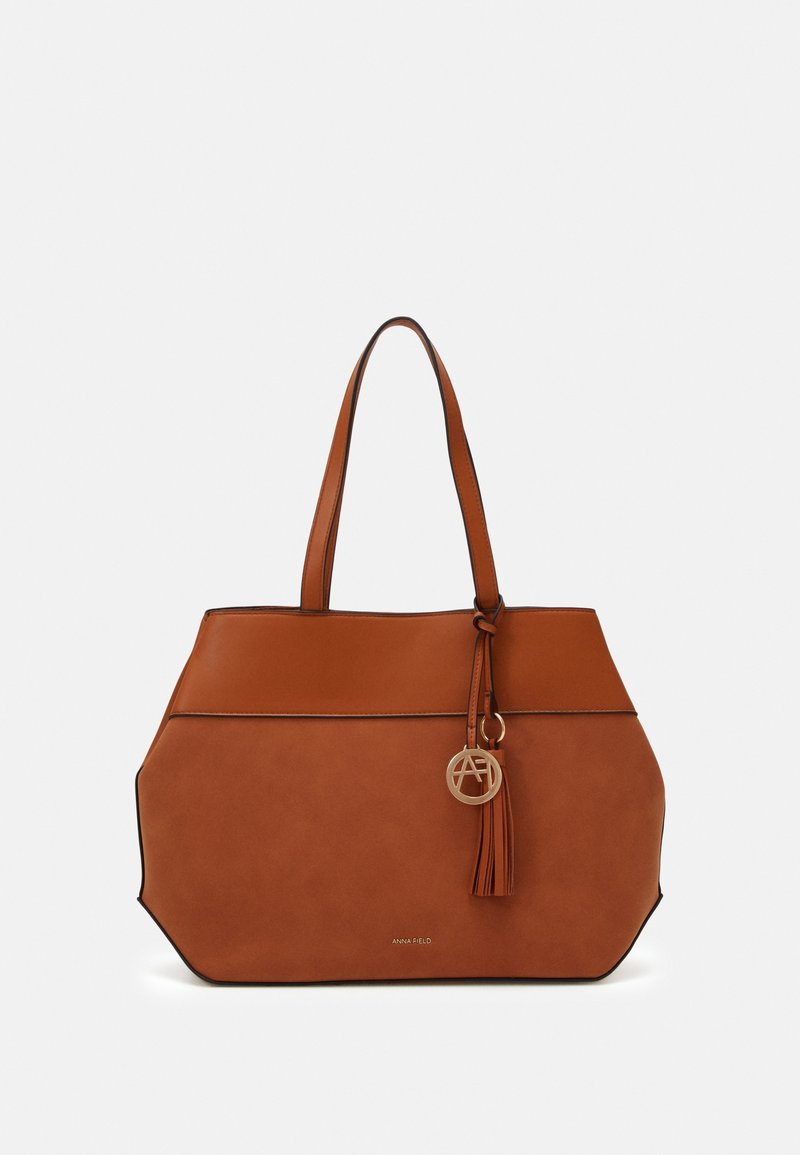 Brun läder tote-väska med en strukturerad form, prydd med en logotypcharm i guldton och fransdetalj, accentuerad med svarta kanter.