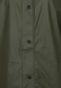 Olijfgroene waterdichte jas met een gladde textuur, drukknoopsluitingen en zichtbare stiksels langs de voorkant en zijzakken.