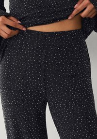 Schwarze Leggings aus strukturiertem Stoff mit weißem Tupfenmuster, ausgestattet mit einem figurbetonten Schnitt und einem breiten elastischen Bund.