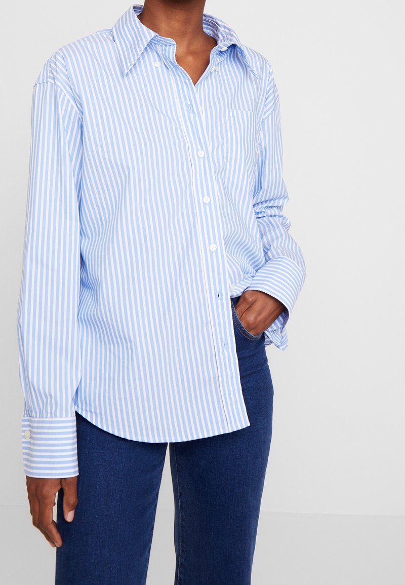Lichtblauw-wit gestreept overhemd met knoopsluiting, kraag, lange mouwen en een borstzak, gecombineerd met donkerblauwe spijkerbroek.