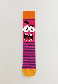 Calcetines hasta la rodilla a rayas rosas y moradas con un puño naranja, con la cara de un monstruo de dibujos animados con ojos grandes y dientes afilados.