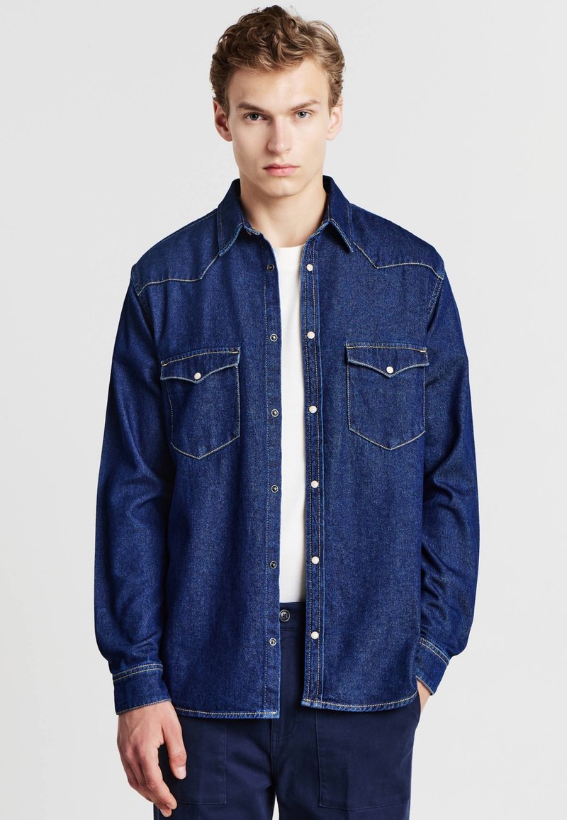 Camicia in denim blu scuro con due tasche sul petto, design con bottoni e cuciture a contrasto. Maniche lunghe con polsini abbottonati. Taglio classico.