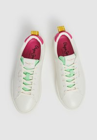 Zapatillas de cuero blancas con acentos en verde y rosa. Presentan un diseño de cordones, una pestaña en el talón amarilla y un logo en la lengüeta. Suela texturizada.