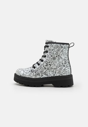 Black and white patterned ankle boots featuring assorted doodles, a thick black sole, round toe, and black laces. Smooth surface with a glossy finish.