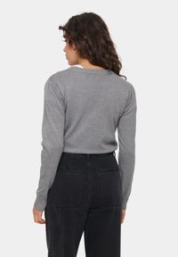 Grauer gestrickter Pullover mit langen Ärmeln und geripptem Halsausschnitt, kombiniert mit hoch taillierten schwarzen Jeans. Hat eine glatte Textur.