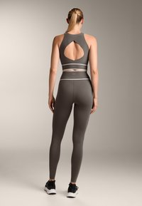 Gray sports bra and leggings set featuring a cut-out back design, textured fabric, and contrasting white bands at the waist and midsection.