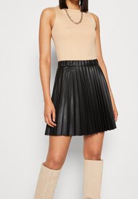 Gonna plissettata nera in faux pelle con cintura elastica, abbinata a un top senza maniche color nude e stivali al ginocchio beige. Collana a catena in argento.