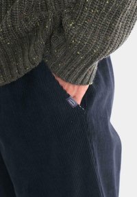 Pantalones de pana azul oscuro con una textura acanalada y un bolsillo lateral; combinados con un suéter de punto grueso en color verde oliva.
