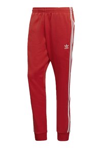 Pantaloni sportivi rossi realizzati in tessuto morbido, con strisce bianche sui lati e un logo ricamato sulla coscia sinistra. Vita elastica con polsini.