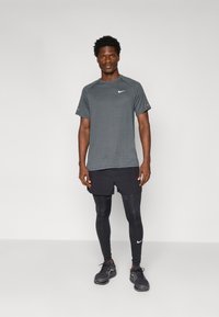 Čierny aktívny set Nike, ktorý obsahuje krátky rukáv, priedušný šedý top a priliehavé čierne legíny, v spojení s čiernymi športovými topánkami.