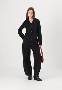Veste en denim noir au design ajusté, avec un ourlet arrondi, deux poches avant, fermeture à bouton, associée à un pantalon en denim noir ample et des bottes à talons.