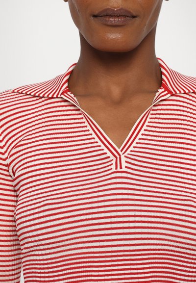 Top en tricot rayé rouge et blanc avec un col en V, présentant des lignes horizontales et une texture côtelée. Tissu avec un léger éclat.