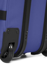 Lila tygresväska med svarta plastdetaljer, två släta svarta hjul och en strukturerad greppyta på handtaget.