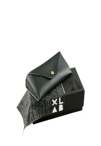 Borsa in pelle nera con chiusura a scatto, posizionata su una scatola nera con motivi geometrici bianchi e un panno per la pulizia con design simili.