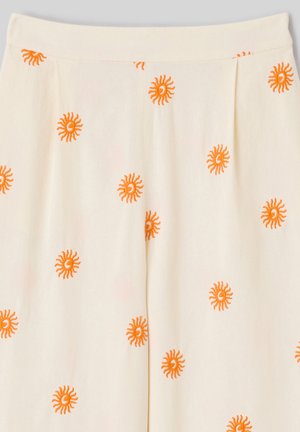 Tissu couleur crème avec des motifs brodés en forme de soleil orange espacés de manière régulière, montrant une ceinture et un détail plissé.