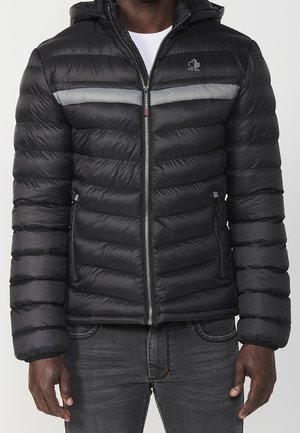 Chaqueta de plumas negra, diseño acolchado con raya gris horizontal, cierre de cremallera, capucha ajustable, dos bolsillos laterales, textura suave.