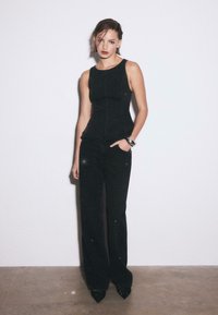 Czarny zestaw dwuczęściowy składający się z dopasowanego, bezrękawnikowego topu i szerokich spodni, ozdobiony subtelnymi błyskotkami, zestawiony z czarnymi butami na szpic.