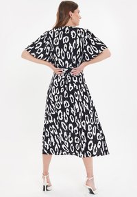 Vestido midi de estampado de leopardo en blanco y negro con mangas cortas abullonadas y detalle de cinta en la cintura, que presenta una Silueta fluida y una textura suave.