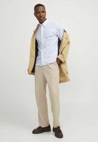 Hellblau-weiße gestreifte Button-Down-Hemden, beige Hosen und einen hellbraunen Mantel. Braune Schuhe mit dekorativen Akzenten vervollständigen das Outfit.