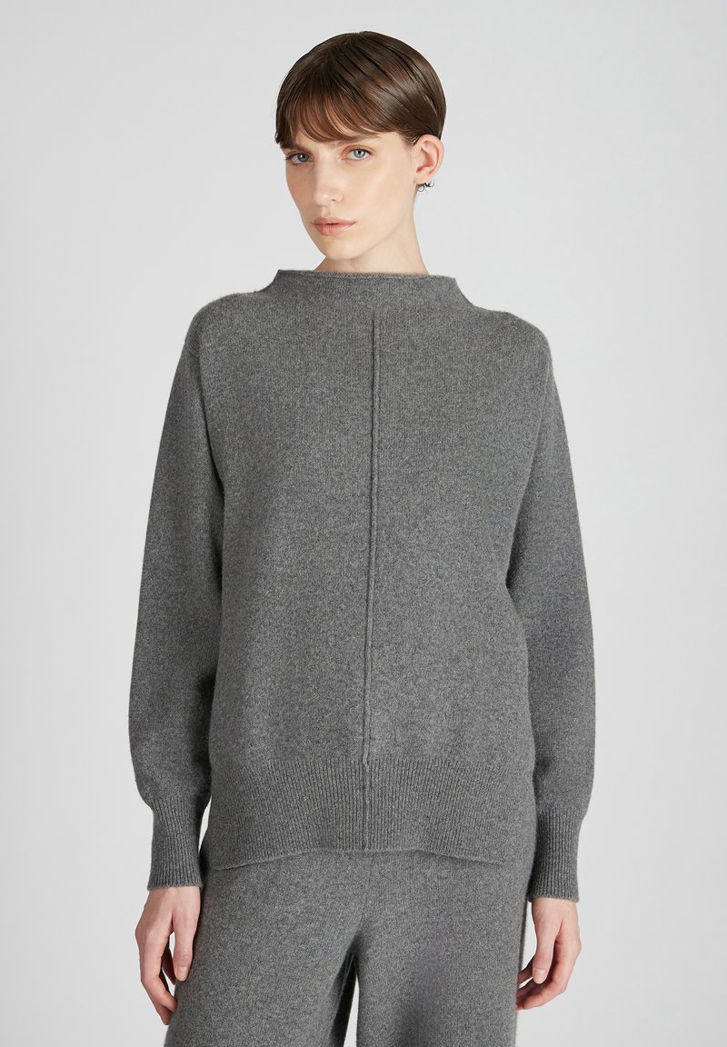 Grauer Wollpullover mit hohem Kragen, überschnittenen Schultern und gerippten Bündchen. Besitzt eine zentrale Rückennaht für zusätzlichen Detail. Weiche Textur.