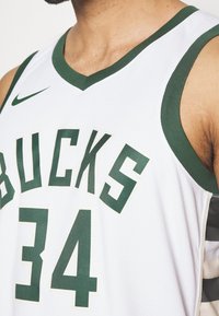 Maillot de basket blanc avec des accents verts et de grandes lettres formant "BUCKS" avec le numéro "34" en dessous. Confectionné en tissu respirant.