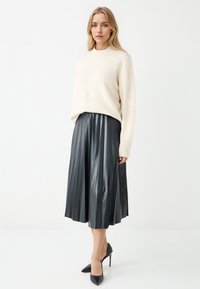 Maglione a maglia crema, gonna midi plissettata in pelle nera e tacchi a punta neri. Texture morbida e design elegante con pieghe definite.