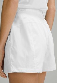 Pantalones cortos blancos con una cinturilla elástica texturizada, bolsillos laterales y costuras visibles, con un ajuste relajado y tela suave.