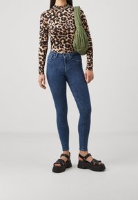 Top de manga larga con estampado de leopardo, vaqueros ajustados azules, sandalias gruesas negras y un bolso de hombro acolchado verde. Diseño simple y entallado.