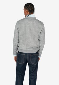 Maglione grigio a maglia con orlo e polsini a coste, indossato sopra una camicia colletto blu chiaro, abbinato a jeans in denim scuro.