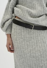 Pulover gri cu model în relief, cu o croială lejeră, asortat cu o curea din piele neagră netedă, dotată cu un cataramă argintie, ce pune în evidență talia.