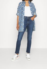 Camisa de flores en tonos azul claro sobre una camiseta blanca, combinada con vaqueros azul oscuro y zapatillas blancas con acentos en gris y naranja.