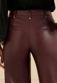 Burgunderfarbene Kunstlederhose mit glatter Textur, hoher Taille, Gürtelschlaufen und zwei Gesäßtaschen. Mit Goldfarbenem Zubehör akzentuiert.