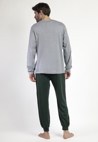 Camisa de manga larga gris con cuello redondeado, combinada con pantalones jogger de cintura elástica verde oscuro. Textura de tela suave, diseño de corte relajado.