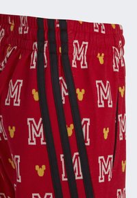 Pantalones cortos deportivos rojos con un patrón de cabezas de Mickey Mouse amarillas y letras "M" blancas por todo el diseño, con franjas laterales negras y una cintura elástica.