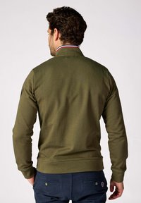 Sweat-shirt olive avec un col montant, des poignets et un ourlet côtelés. Présente une texture subtile et un accent à rayures multicolores sur le col.