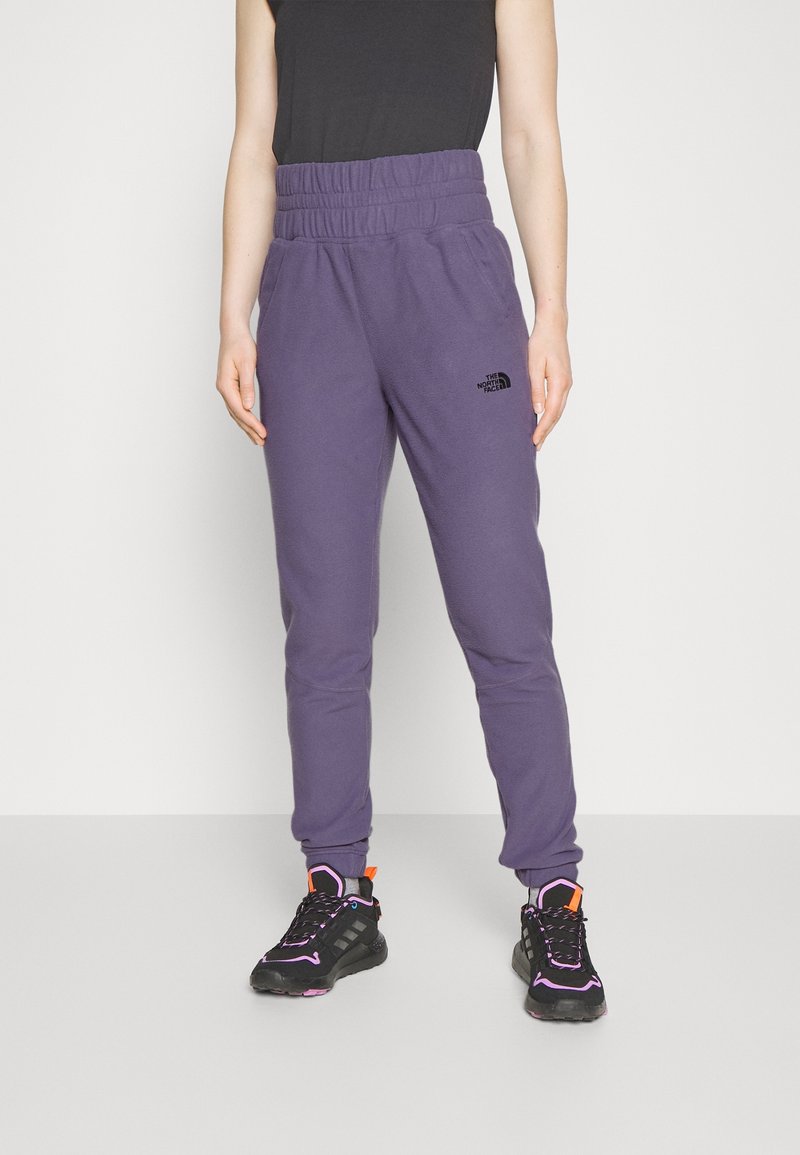 Lila Fleece-Jogginghosen mit elastischem Bund und Seitentaschen, ausgestattet mit einem kleinen schwarzen Logo am linken Bein. Getragen mit schwarzen Sportschuhen.