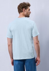 Vaaleansininen lyhythihainen t-paita, joka on valmistettu pehmeästä, teksturoidusta kankaasta. Siinä on pyöreä pääntie ja hieman käännetyt hihansuut, käytettynä sinisten housujen kanssa.