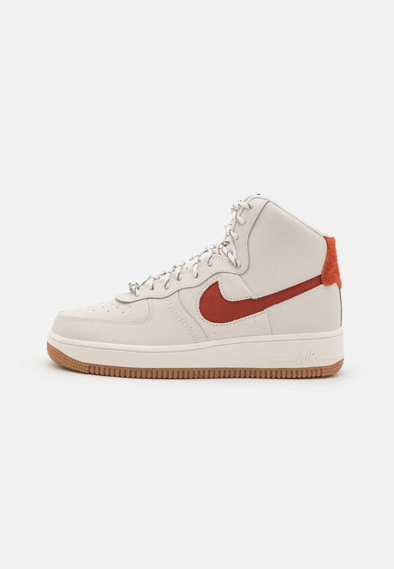 Baskets montantes en cuir crème clair avec un Swoosh rouge, un dos texturé orange et une semelle en caoutchouc naturel. Caractéristiques œillets et lacets en argent.