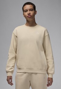 Felpa beige con polsini e scollatura a costine, caratterizzata da un piccolo logo ricamato bianco sul petto, realizzata in tessuto morbido e testurizzato.
