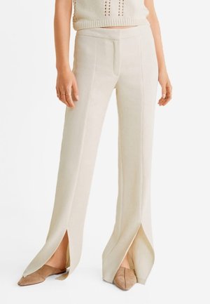 Pantalones de pierna ancha color crema con aberturas en el dobladillo, que presentan una textura suave y detalles de costura vertical, combinados con zapatos beige.
