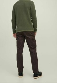 Vihreä teksturoitu neule, joka on yhdistetty tummiin cargo-housuihin, joissa on sivutaskut. Mustat kengät täydentävät asua. Neutraali tausta.