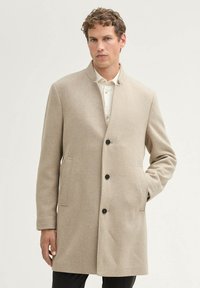 Beige Wolle-Mix Mantel, gerader Schnitt mit Stehkragen, zwei seitlichen Taschen und drei schwarzen Knöpfen, strukturierter Stoff mit einem dezenten Muster.