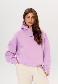 Hoodie oversize lilla realizzato in tessuto morbido, con tasca a marsupio e logo ricamato sul petto. Texture liscia e vestibilità comoda.