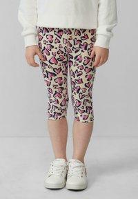 Legginsy z beżowym tłem, zdobione różowymi i czarnymi wzorami serc. Krótkie długości i miękka tkanina. W zestawie z białymi sneakerami.