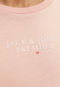 Lichtroze katoenen t-shirt met een ronde halslijn en een gestructureerde opdruk van "JACK & JONES PREMIUM" in het wit, vergezeld van een geregistreerd handelsmerk symbool.